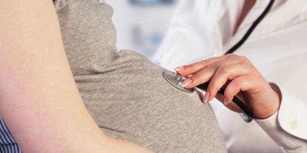 A doctor places a stethoscope on a pregnant woman's stomach.