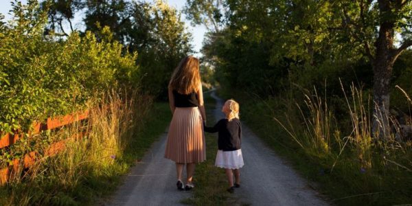 A woman and a child holding hands on a country footpath