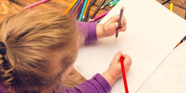A young girl colours in a blank sheet of paper with pencils.