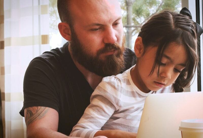 A man and a girl sit at a laptop together.